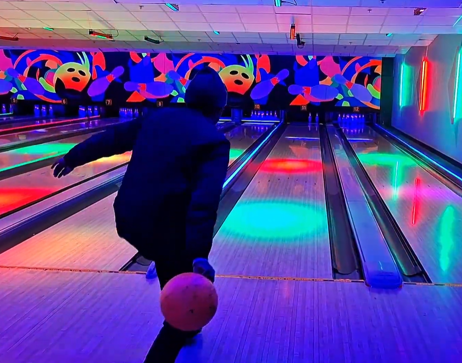 A person bowling in a neon-lit bowling alley
